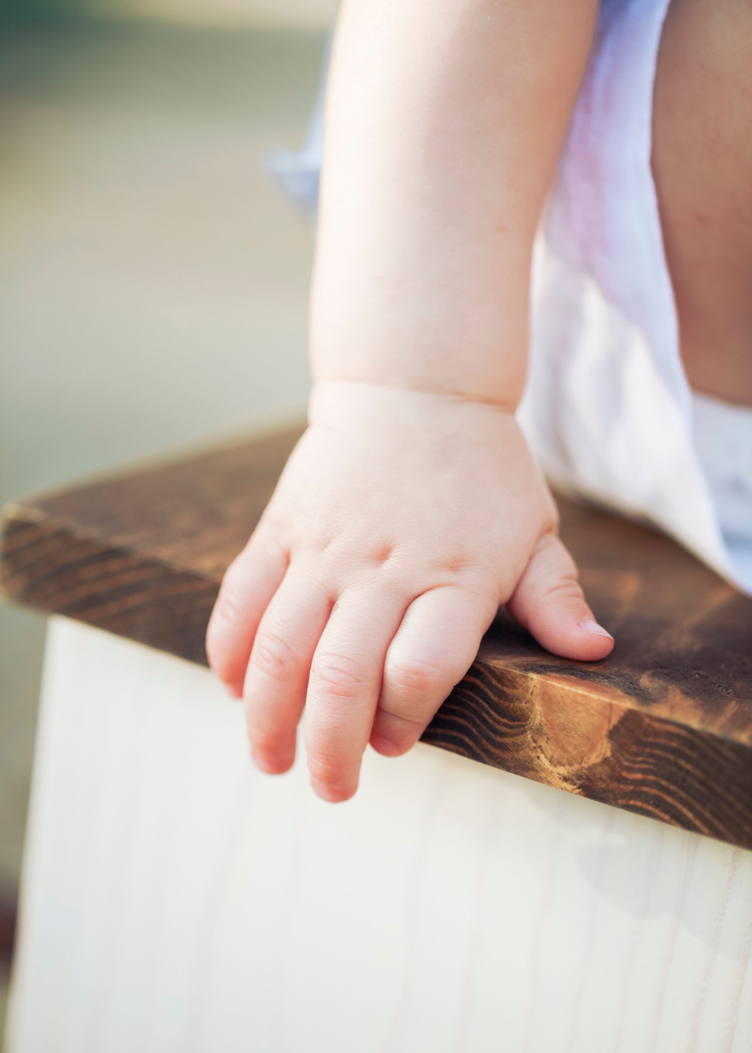Close-up of a small child's hand resting on a dark wooden surface.