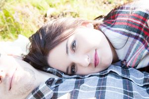 Person lying on plaid blanket in soft natural lighting during outdoor photo session.