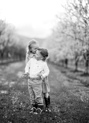 Two small children share a sweet moment in a black and white orchard setting.