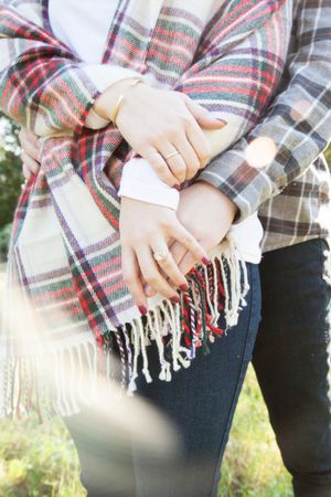 Close-up detail of hands holding plaid blanket with fringe during outdoor portrait session.