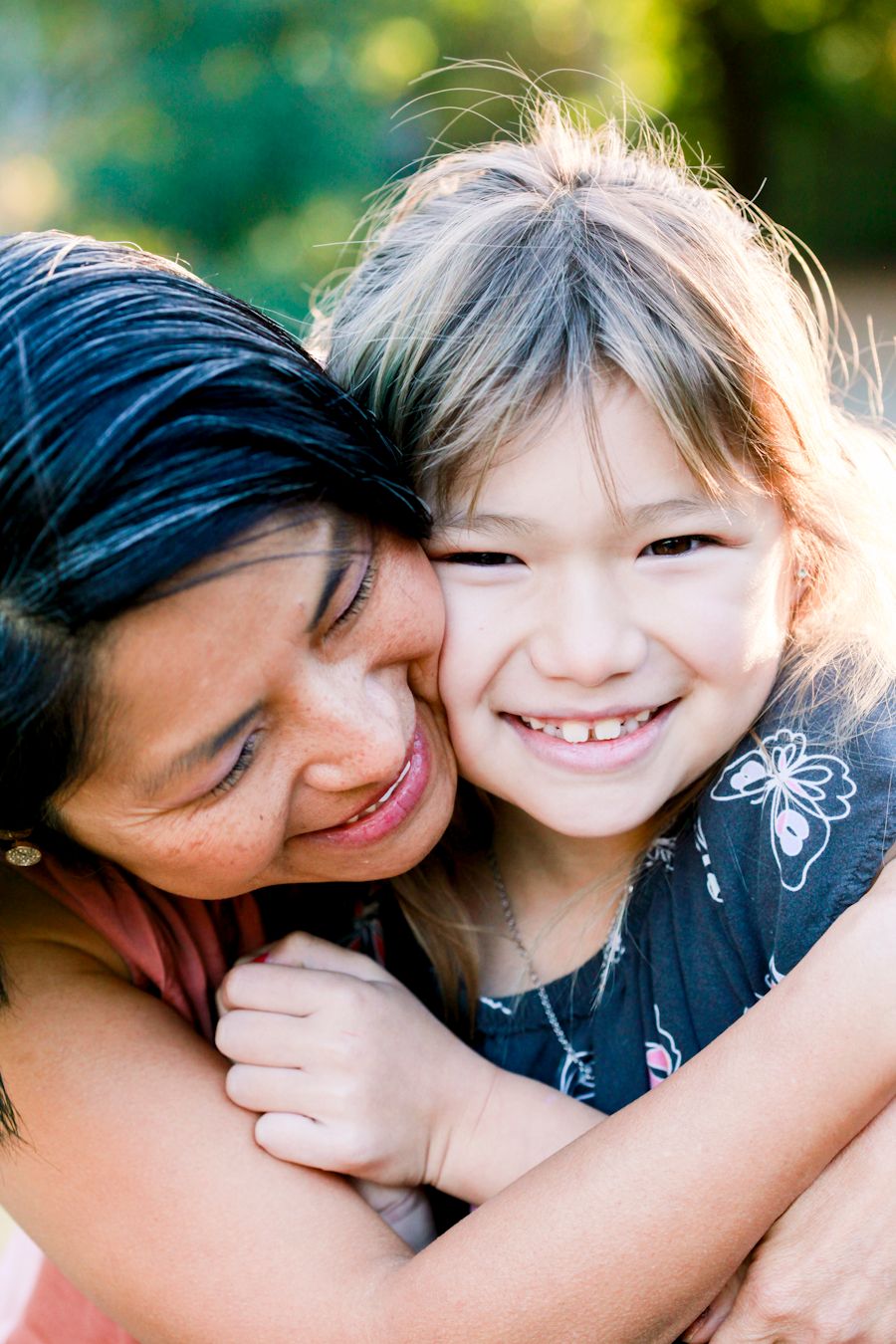 Two people share a tender embrace while smiling warmly in natural outdoor lighting.