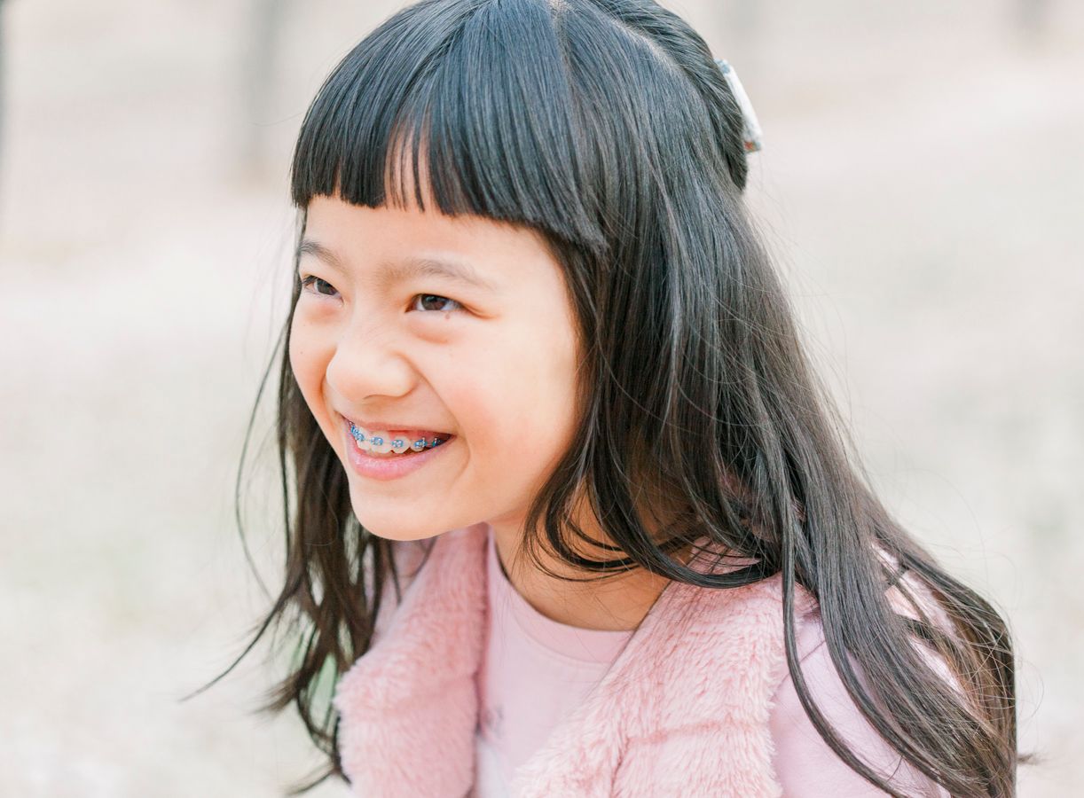 A person in a pink sweater smiles joyfully against a soft neutral background.