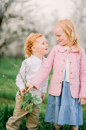 Two children in spring attire interact playfully among blooming trees.