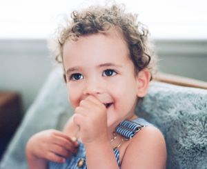 Young child with curly hair resting on soft gray cushion in natural window light.