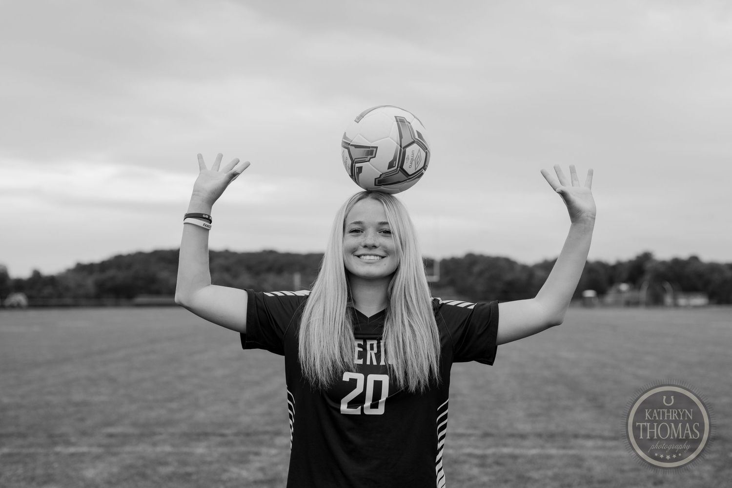 Black and white photo of player balancing soccer ball while raising arms on field.