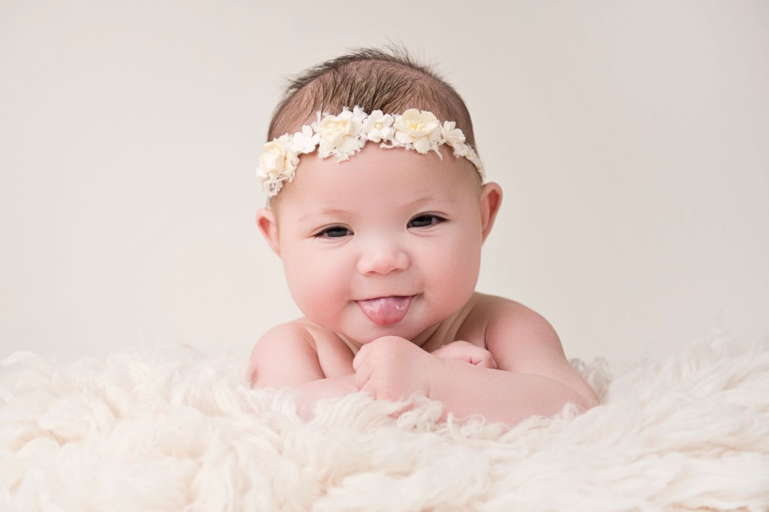 Baby wearing delicate floral headband lying on white fluffy blanket in studio portrait.
