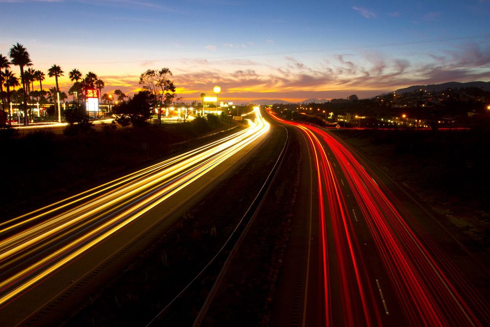Long exposure of highway at sunset showing red and yellow light trails.