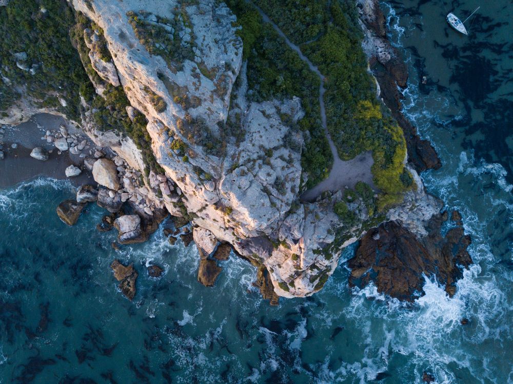 Dramatic aerial view of rocky coastline where rugged cliffs meet churning ocean waves.
