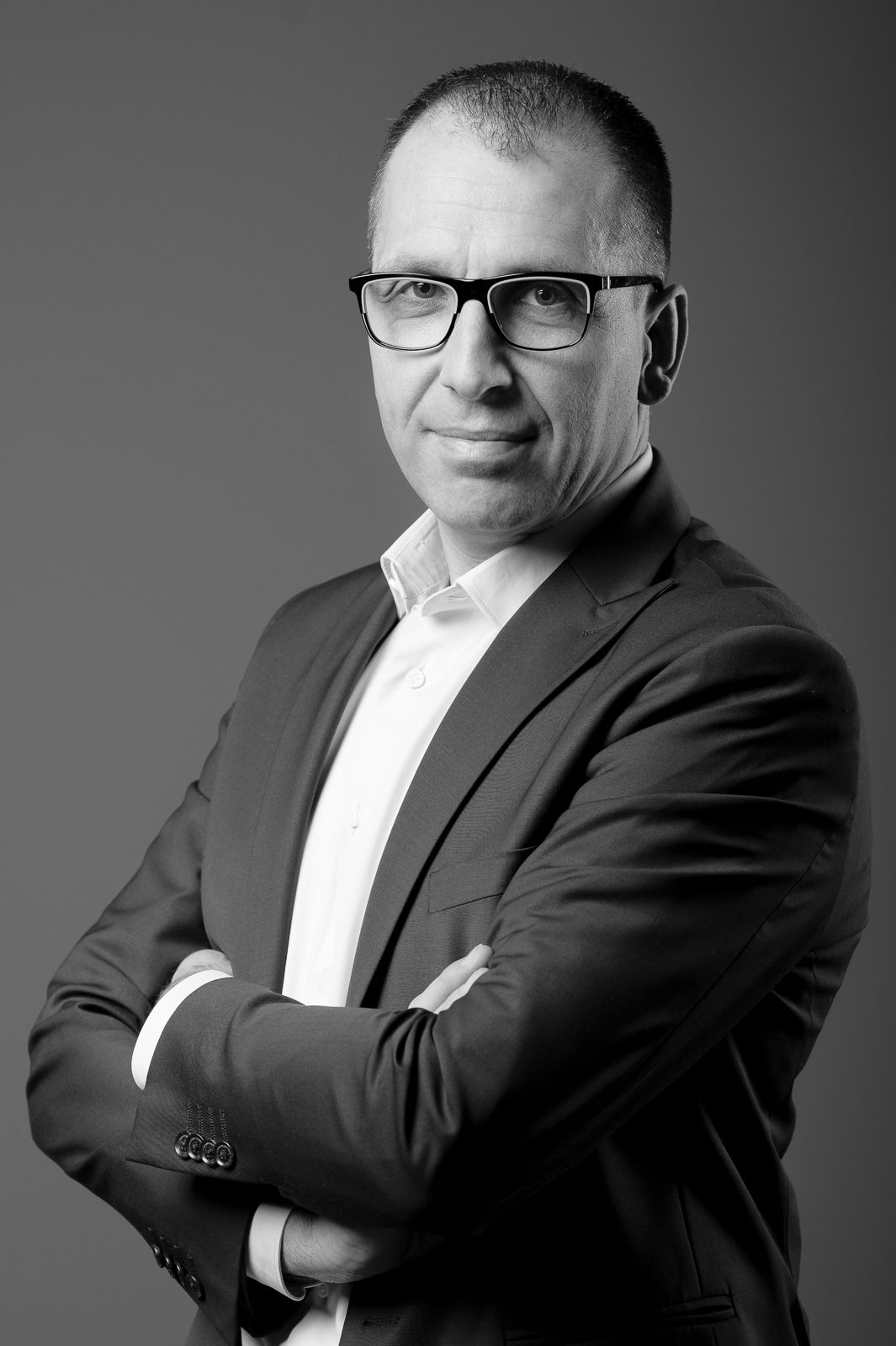 Professional black and white portrait of a businessman in glasses and suit against gray background.