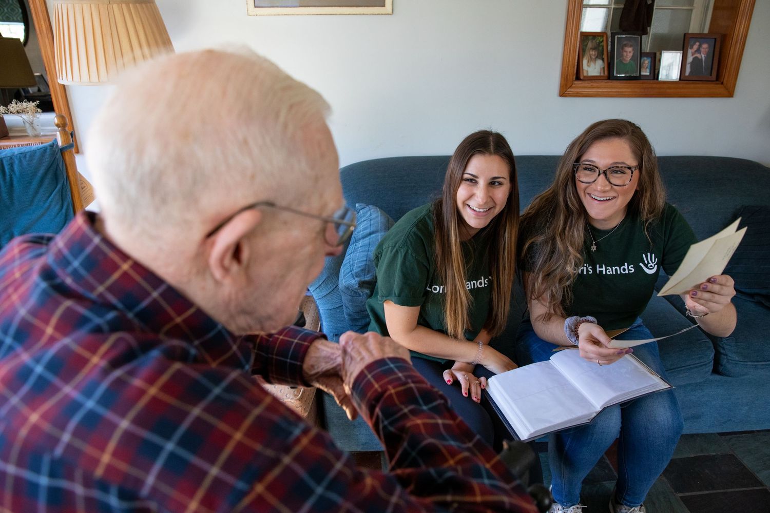 Students reviewing old photos and a scrapbook with an elderly man in plaid on a blue couch.
