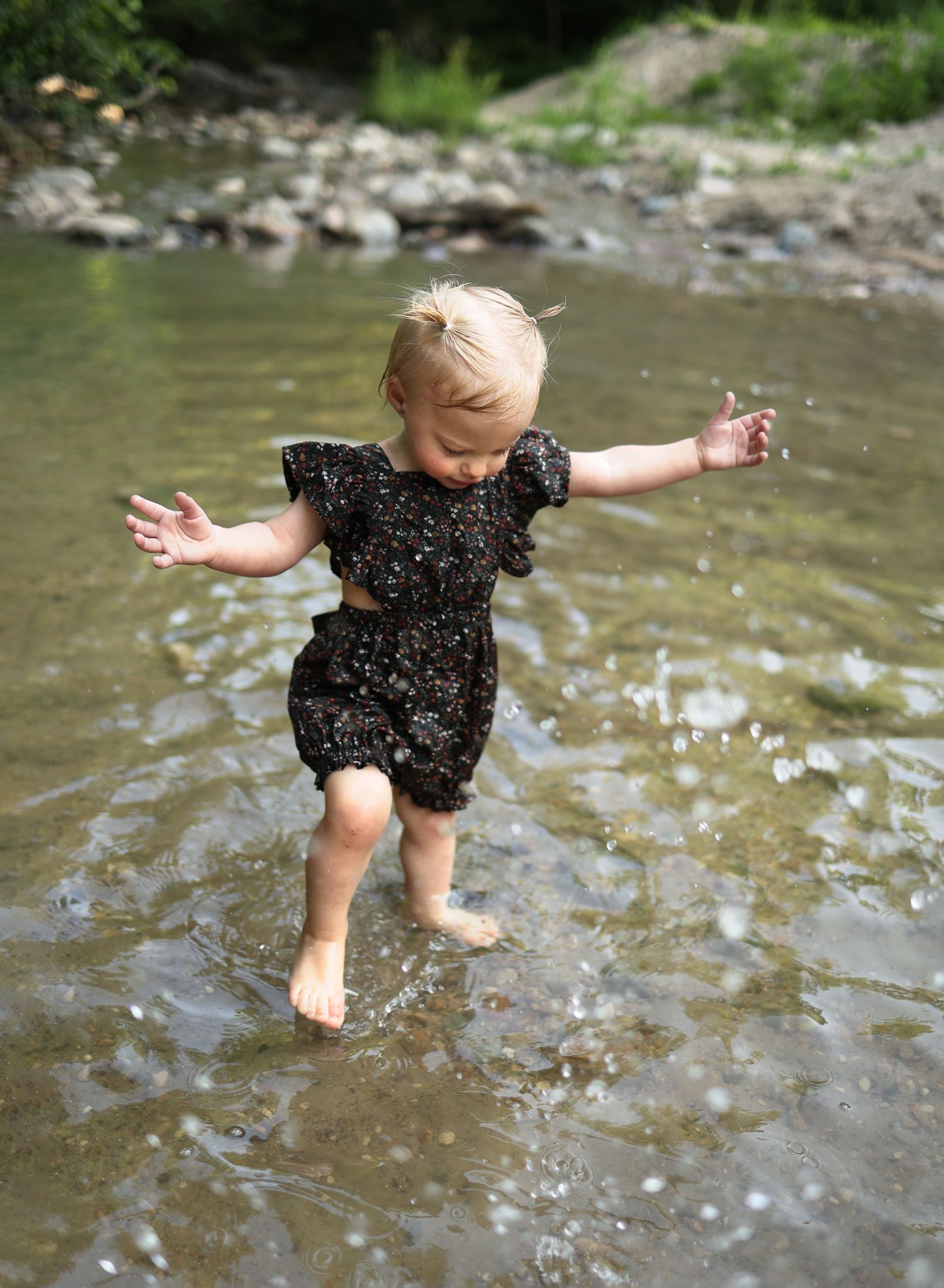 Joyful splashing in a shallow creek wearing a black polka dot romper.