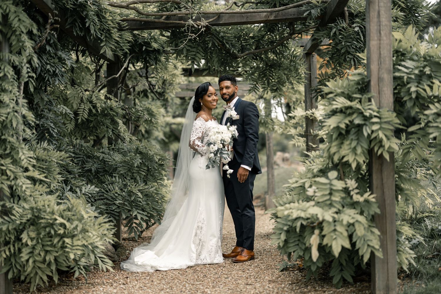A romantic wedding photo of a couple embracing under a lush green garden archway.