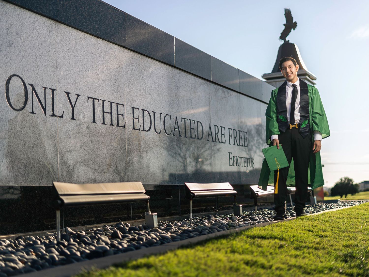Graduate poses by inspirational quote wall wearing green academic regalia.