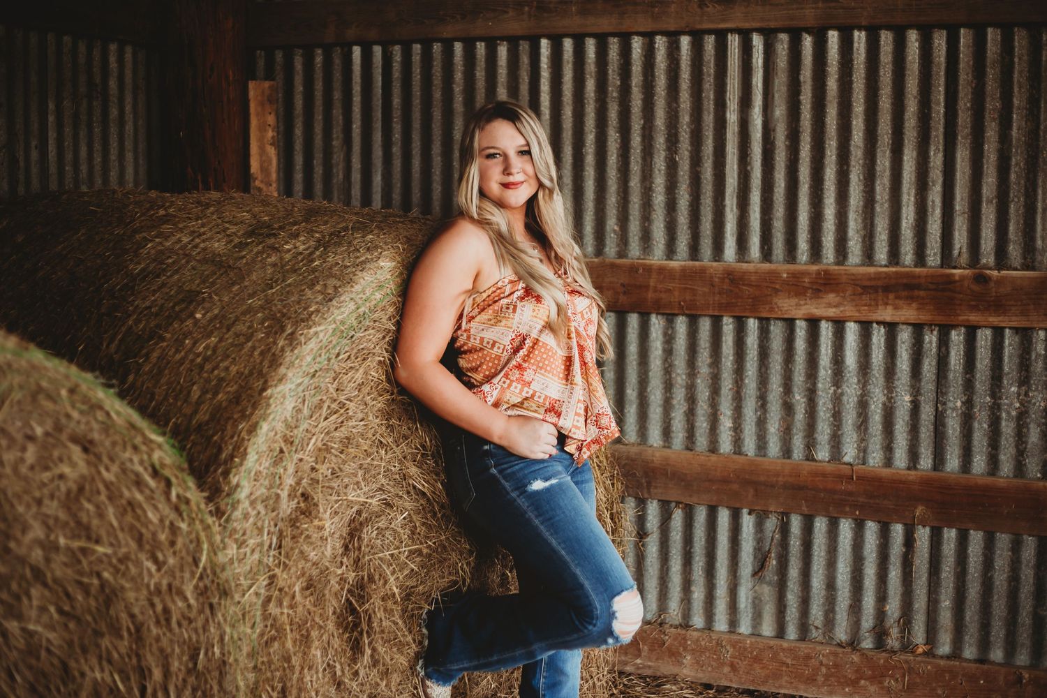 A casual portrait session against a rustic barn wall with hay bales.