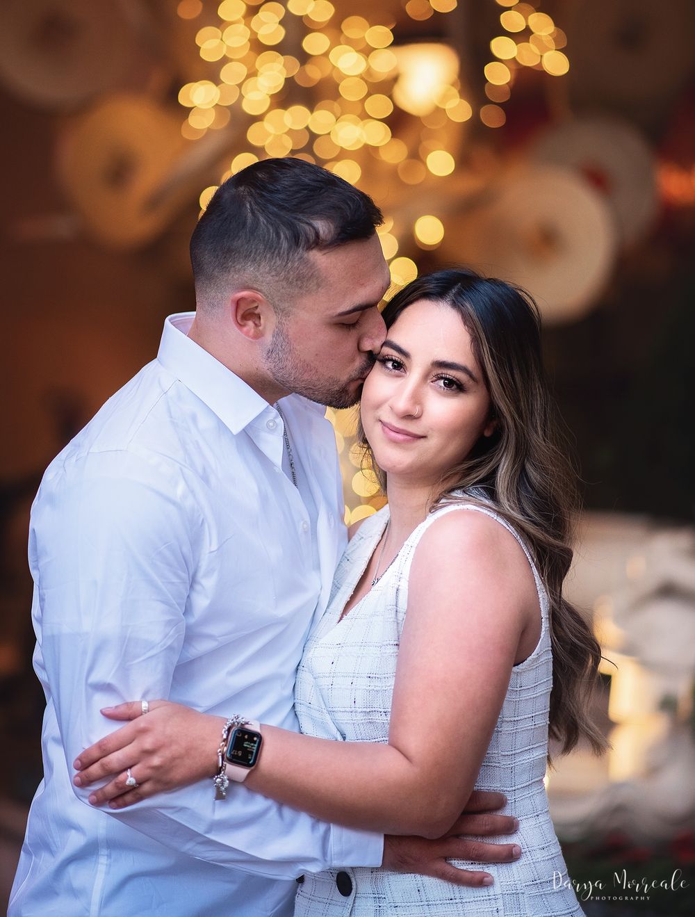 Romantic couple embracing in soft golden bokeh lighting during engagement photoshoot.