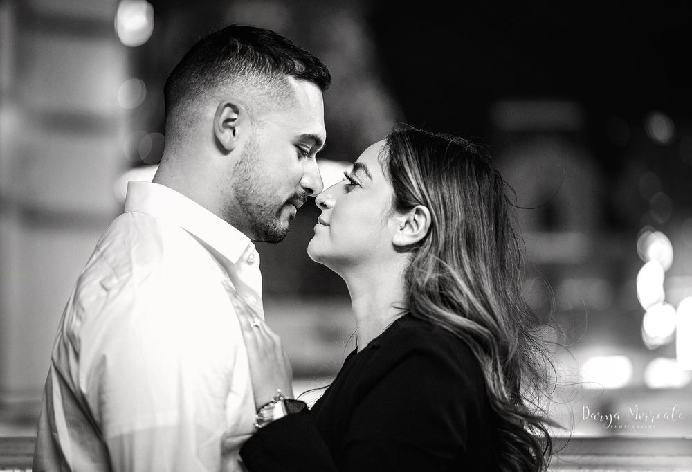Intimate black and white portrait of couple in romantic pose with city lights in background.