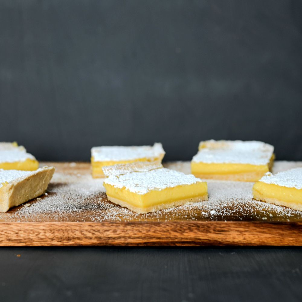Lemon bars dusted with powdered sugar displayed on a wooden serving board.