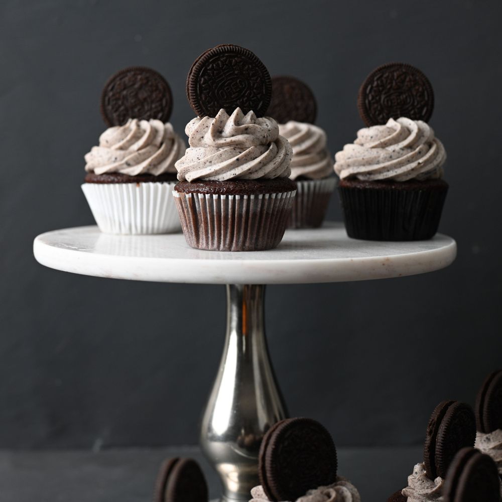 Cookies and cream cupcakes displayed on a white pedestal cake stand against a dark background.