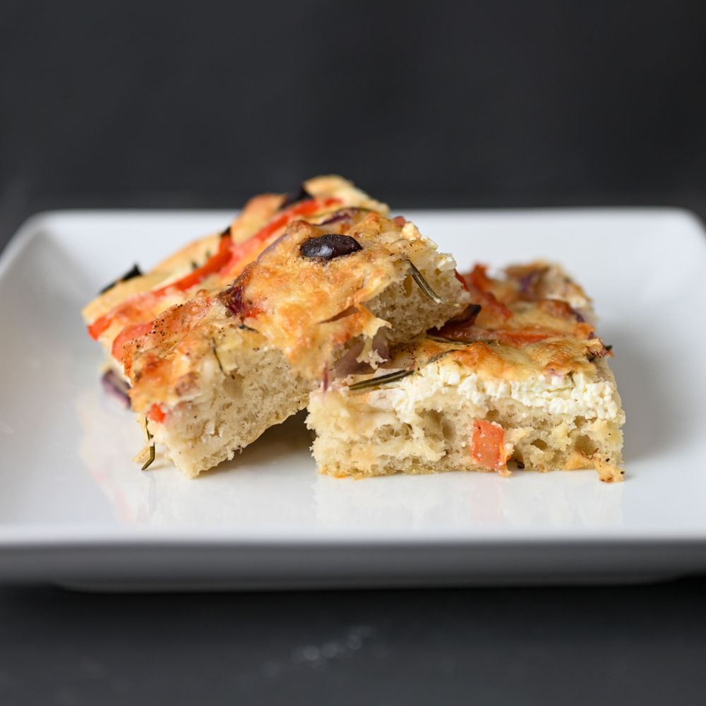 Sliced focaccia bread with herbs and tomatoes on a white plate against a dark background.