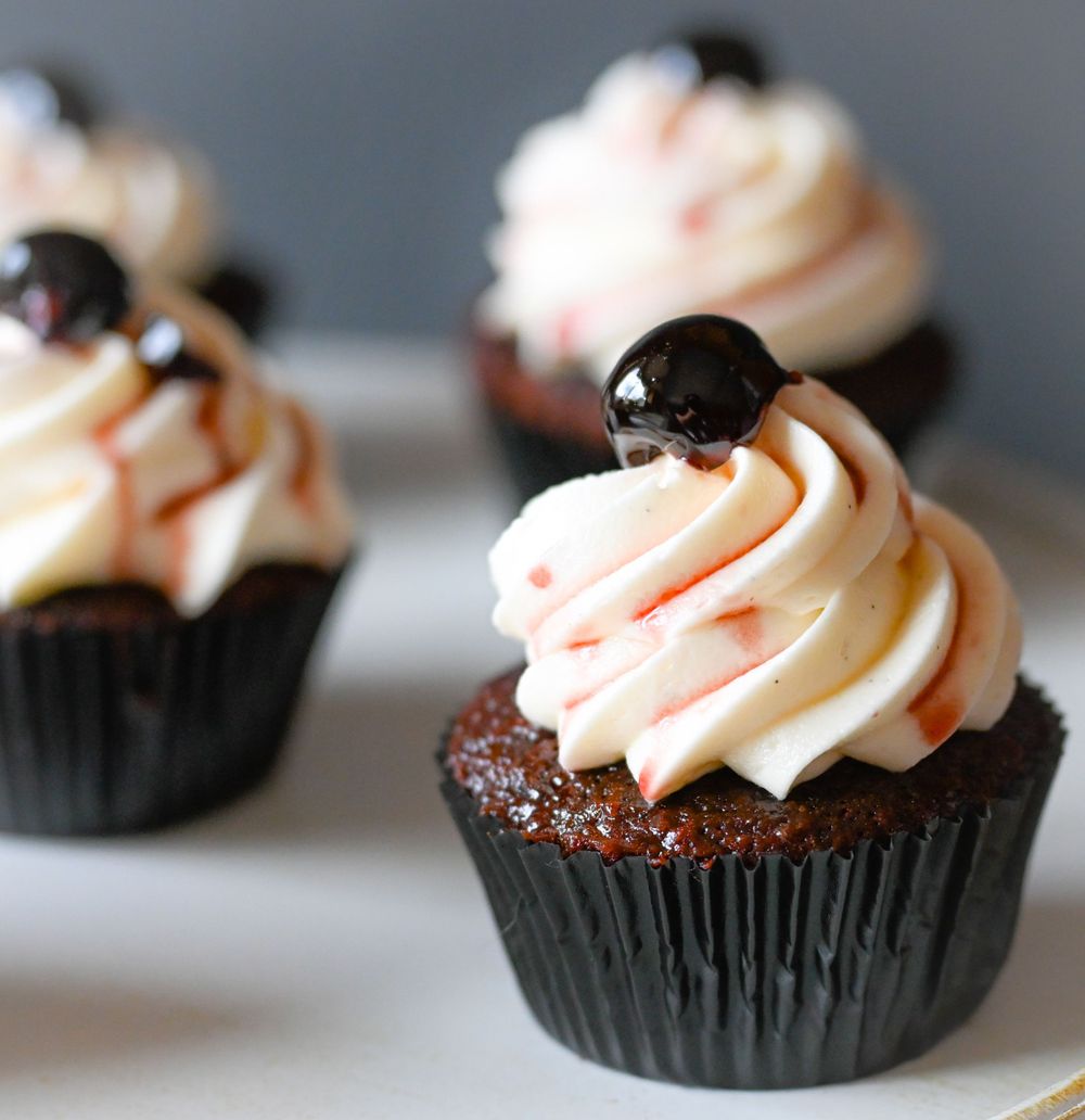 Chocolate cupcake topped with swirled peach frosting and dark chocolate garnish in a black paper liner.