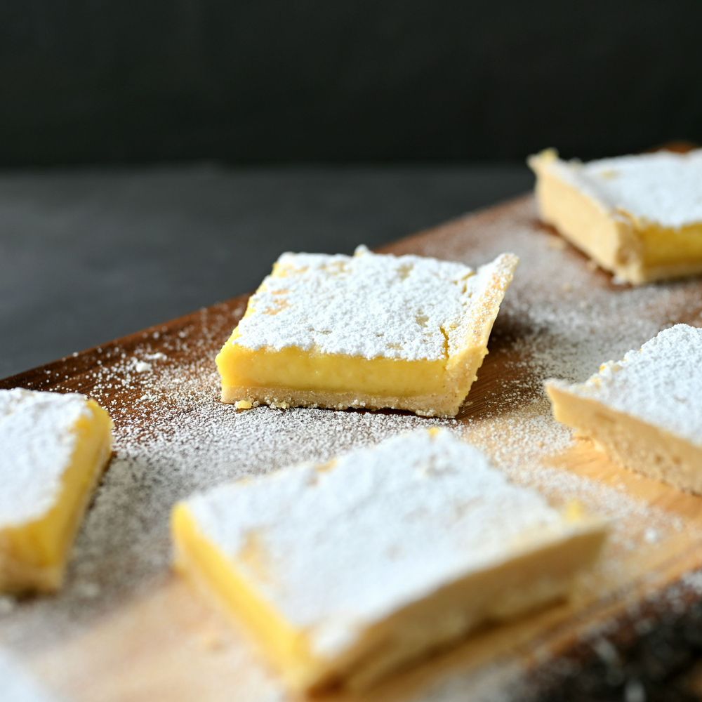 Homemade lemon bars with powdered sugar topping on a rustic wooden surface.