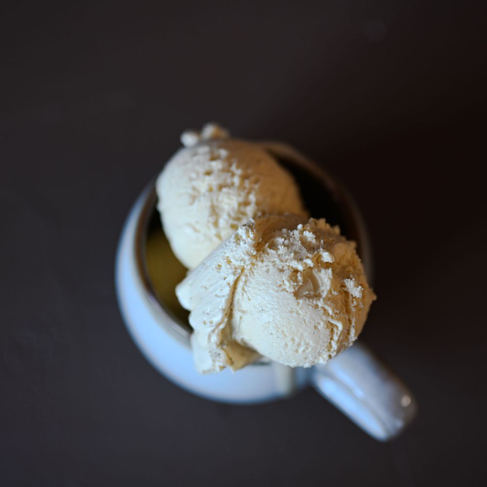 Three scoops of vanilla ice cream served in a white ceramic mug against a dark background.