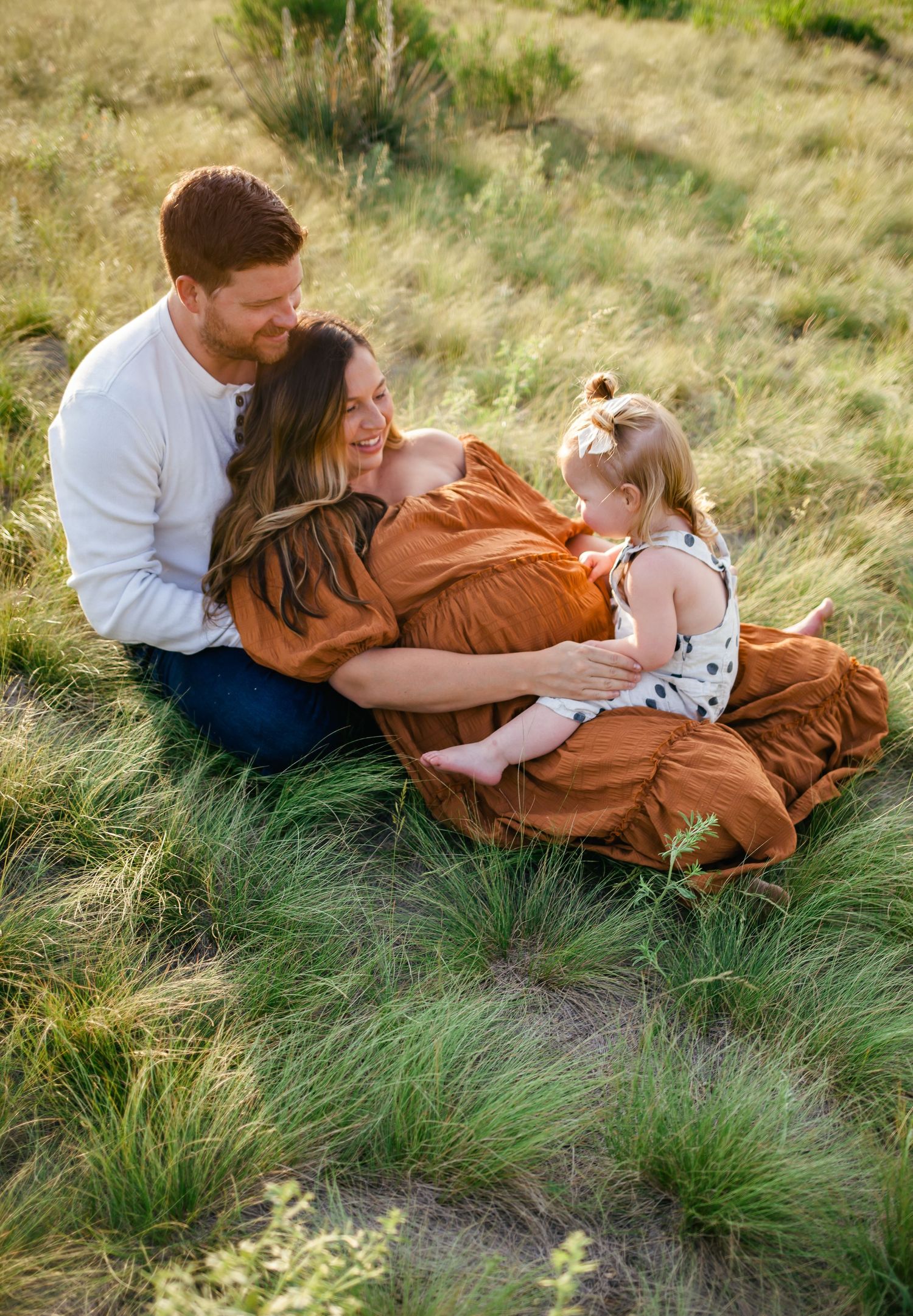 Family enjoying tender moment together while sitting in tall grass during golden hour. Denver family Photography.