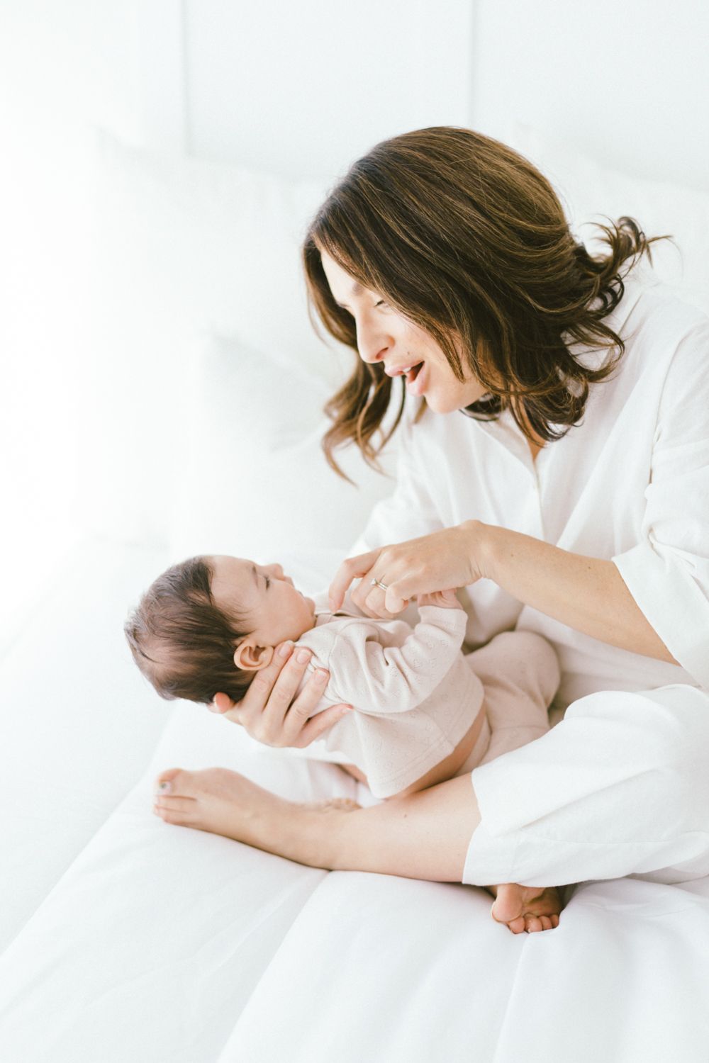 Playful bonding moment between parent and baby on white bedding.