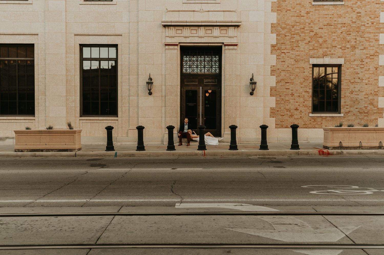 Long exterior view of a classic brick and stone building facade with vintage lampposts.