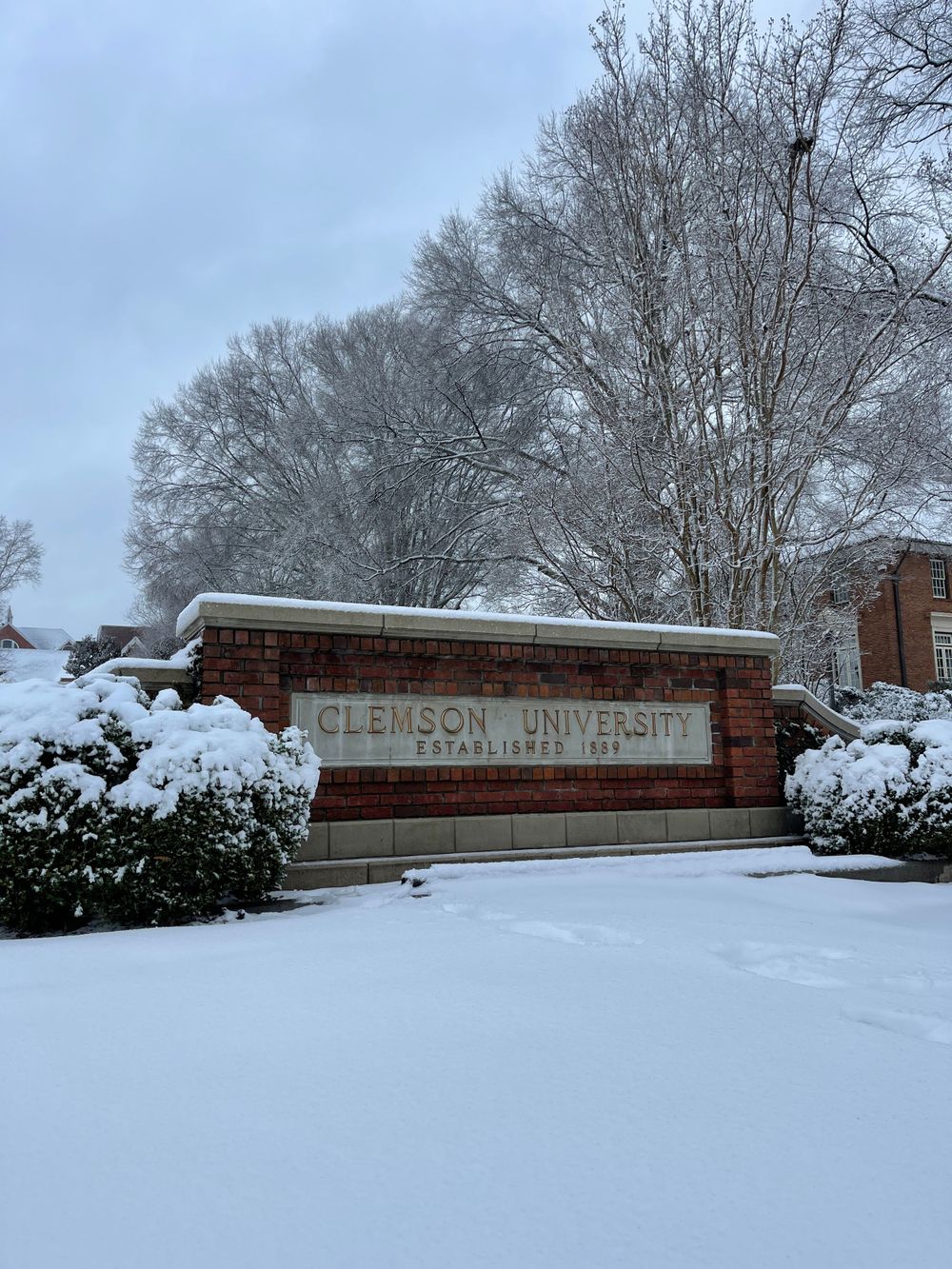 Snow-covered Clemson University entrance sign surrounded by winter landscape.