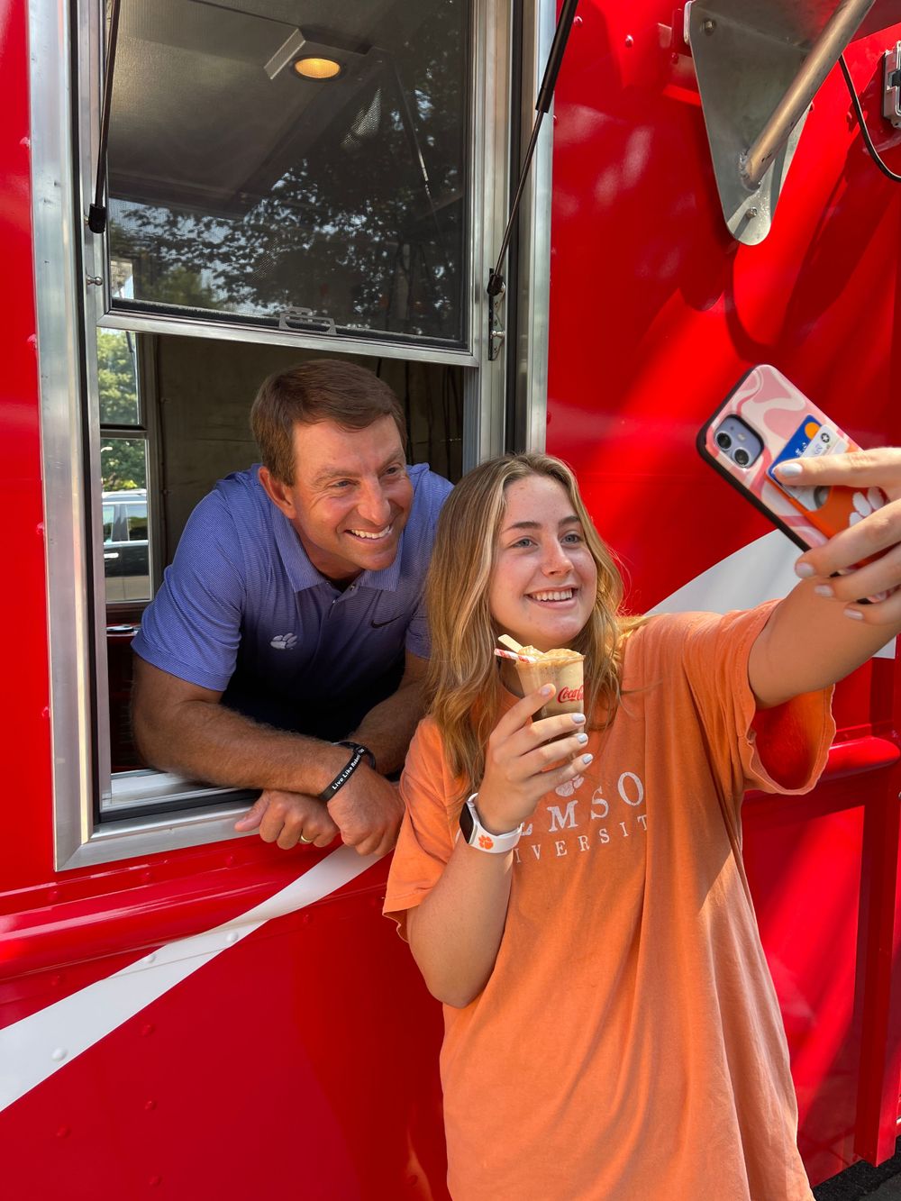 Two people taking selfie at red food truck window while enjoying ice cream.