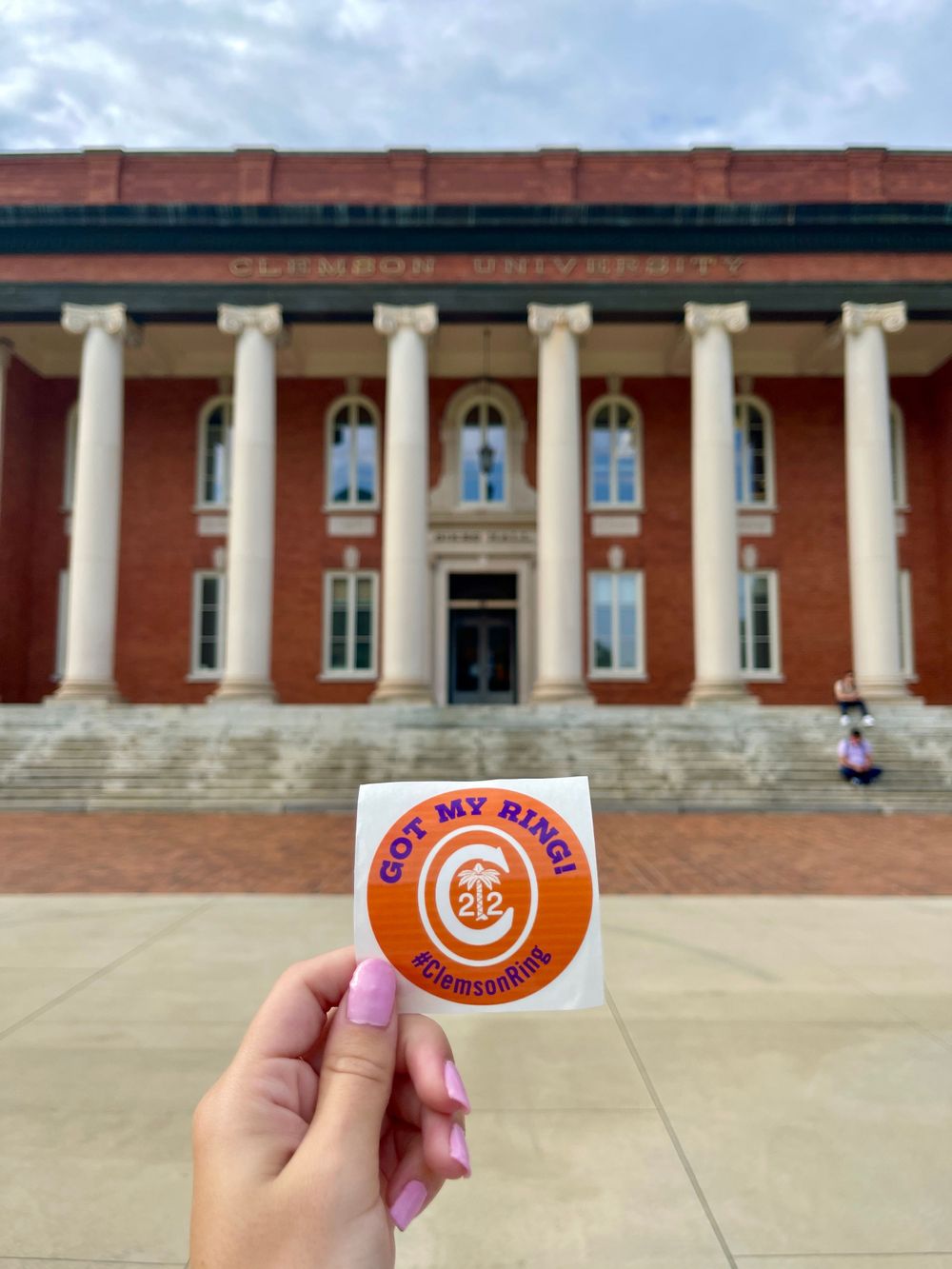 Person holding Clemson pride sticker in front of historic brick building with white columns.