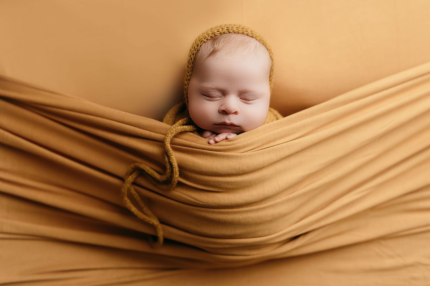 Newborn baby wrapped in caramel colored fabric during artistic portrait session.