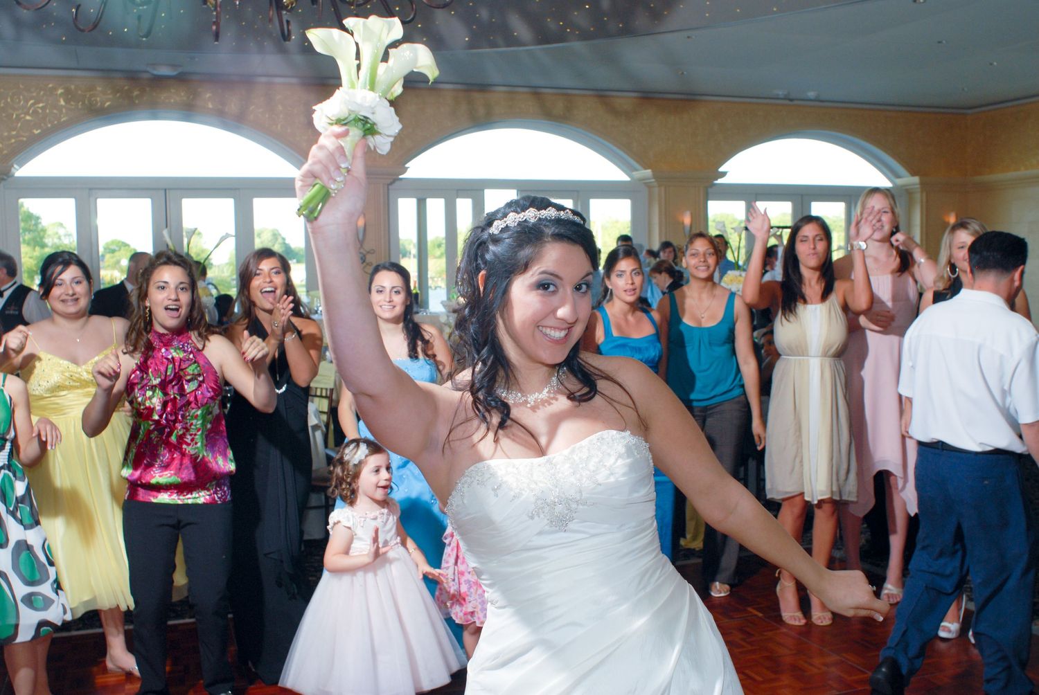 People celebrating at a wedding reception as a bride holds up a bouquet in a festive indoor venue.