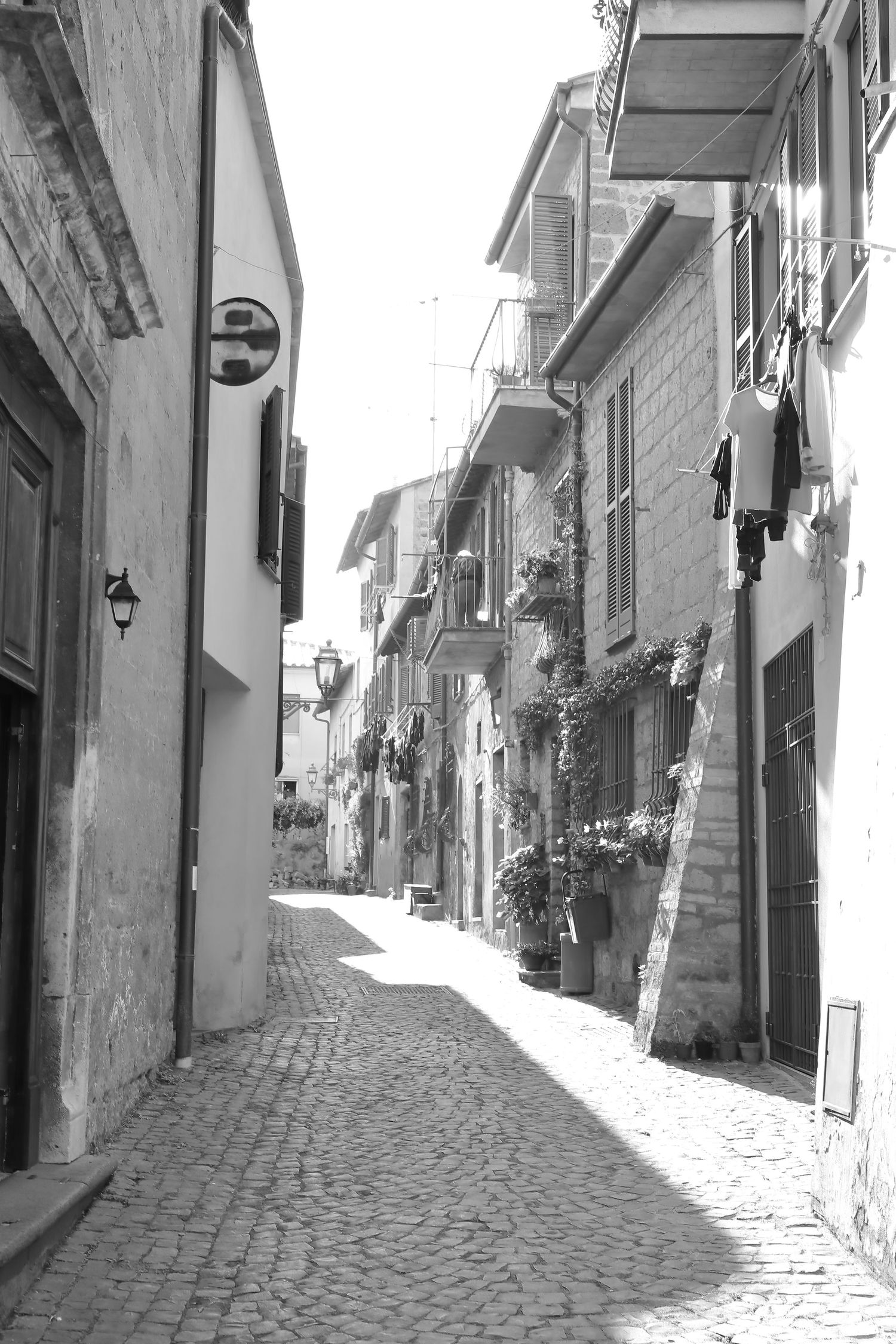 Narrow cobblestone alley with traditional Italian architecture and hanging laundry in black and white.