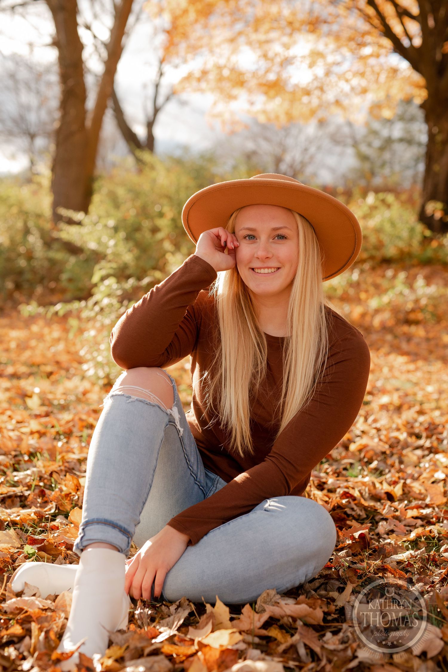 Casual autumn portrait of someone sitting on fallen leaves wearing brown sweater and hat.