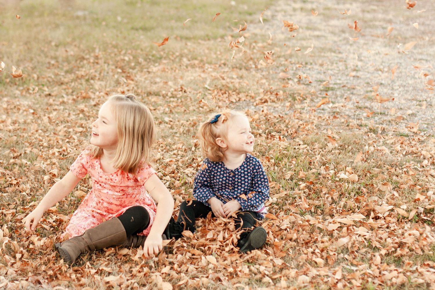 Two children play together in a pile of autumn leaves on the ground.