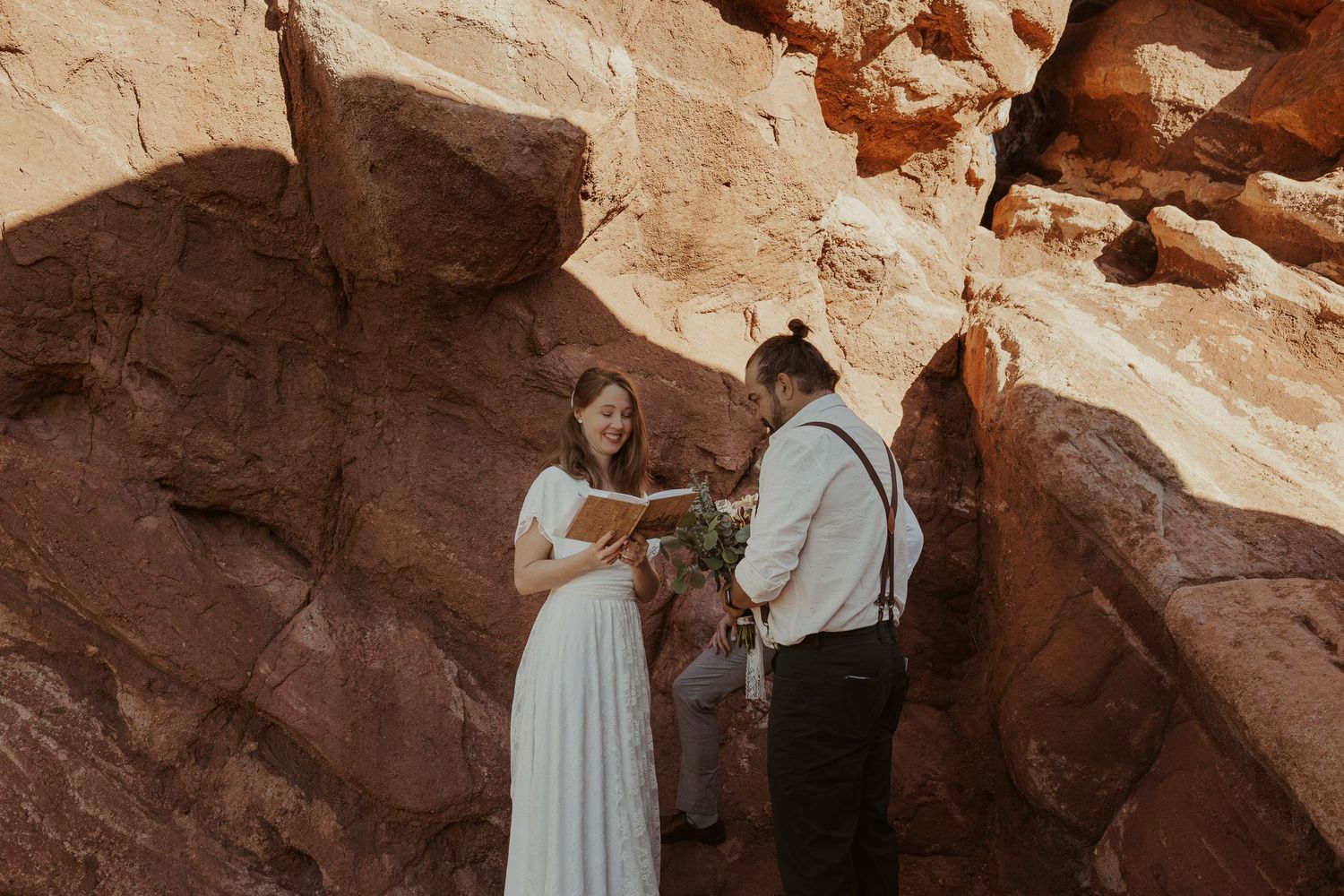 an elopement ceremony taking place in a nook of rock formations with the bride smiling during her vow reading