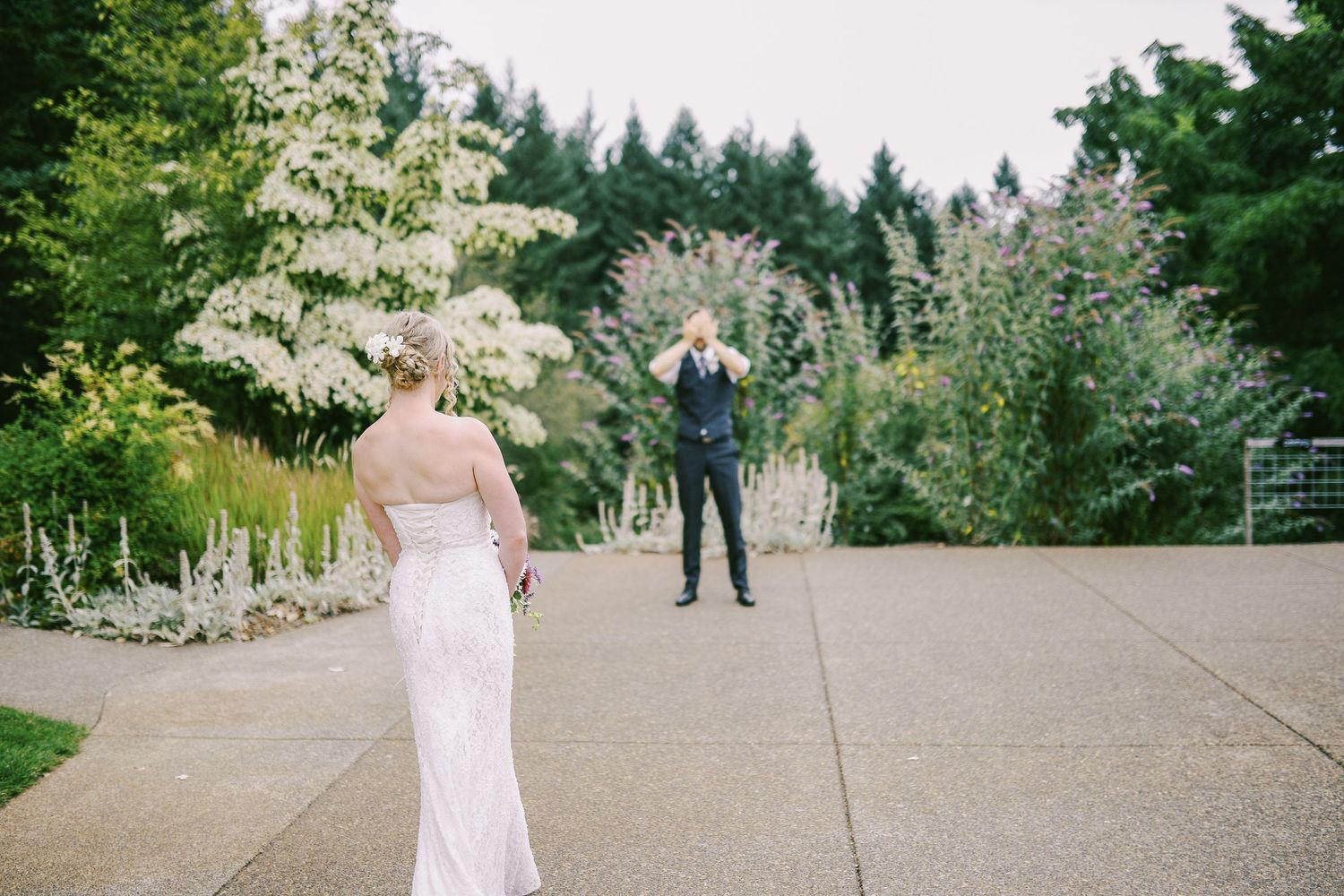 A romantic first look moment between a couple on a garden pathway surrounded by lush greenery and flowers.