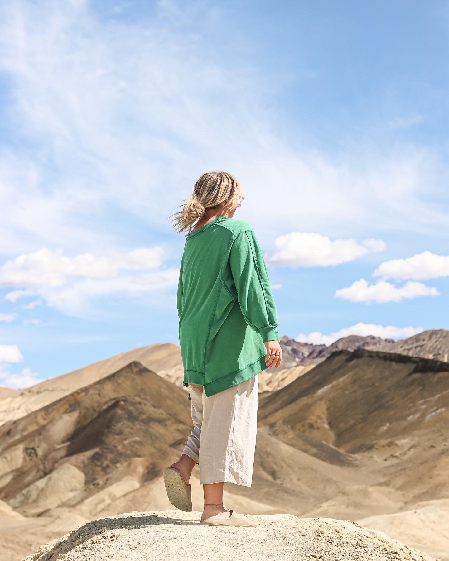 Cora Emilie Media A person in green hoodie stands on a hill overlooking desert mountains.