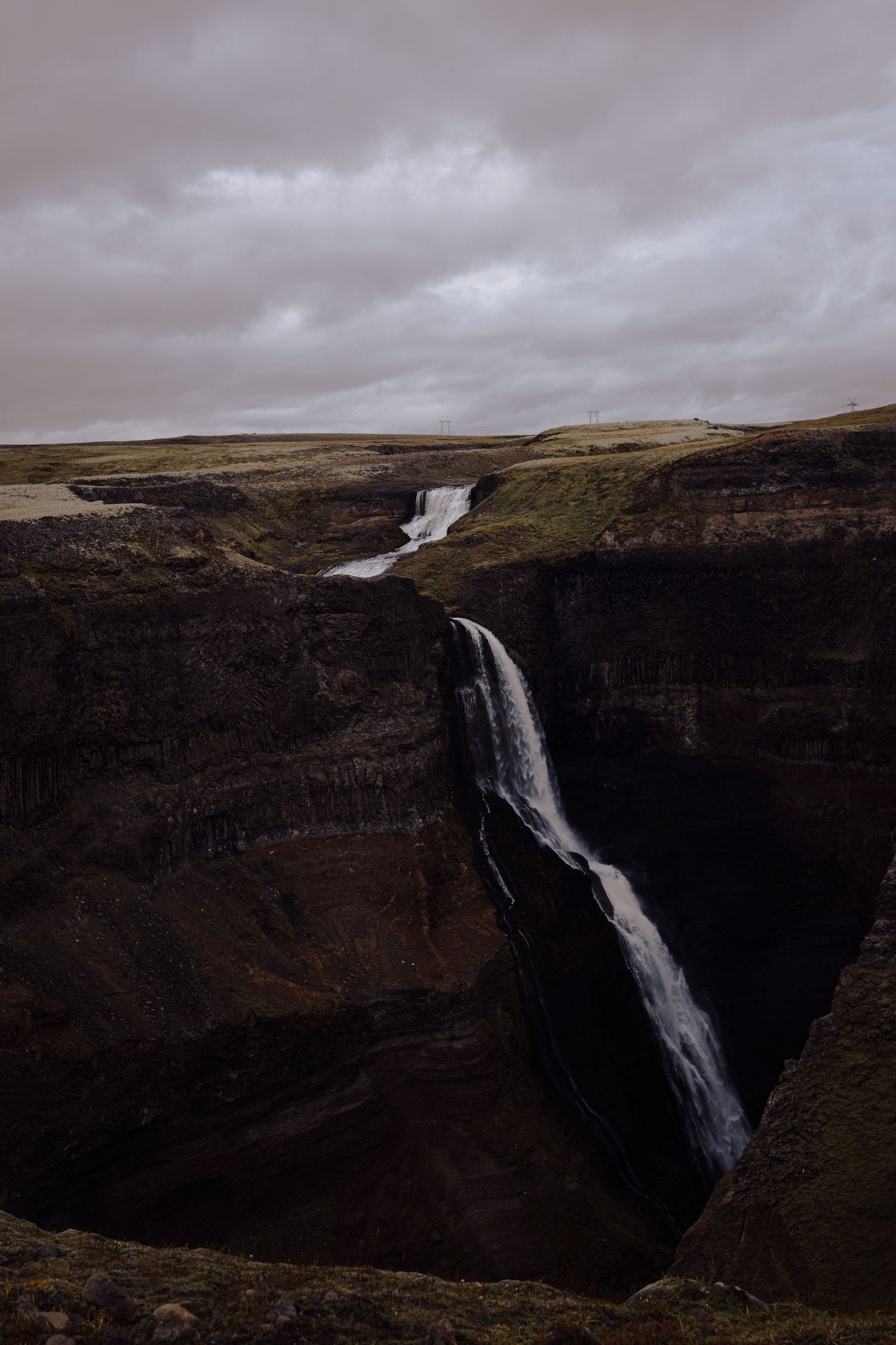 Dramatic waterfall cascading down dark rocky cliffs under moody overcast sky.