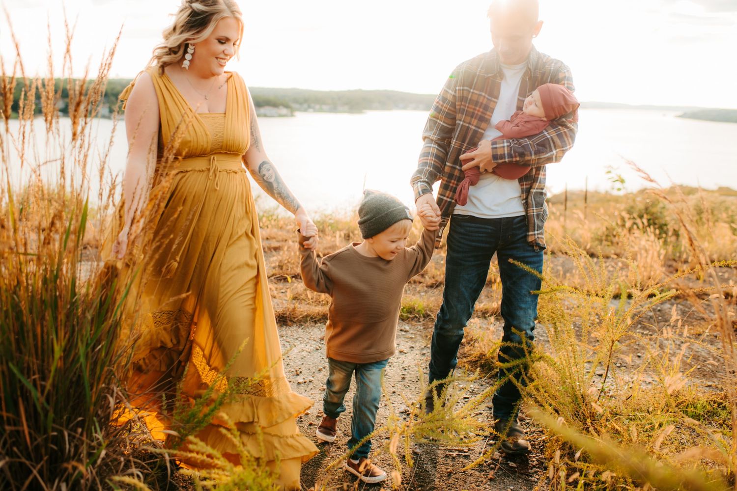 A family walks together through golden grasses at sunset by a serene lake.