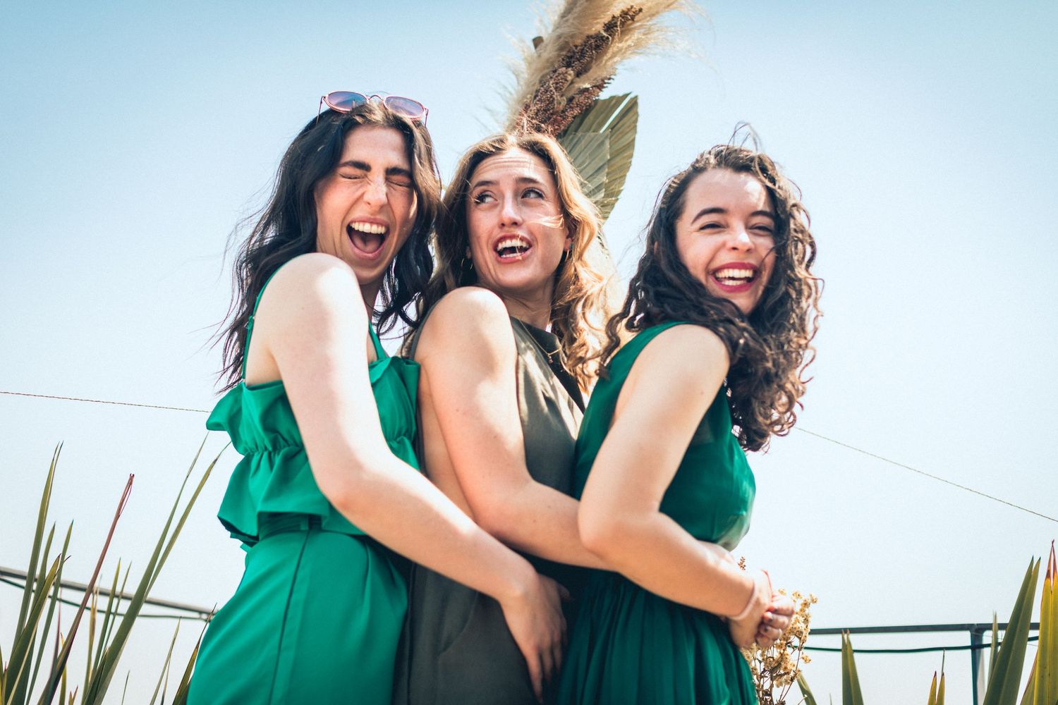 Group of friends in matching emerald green dresses laugh joyfully together outdoors.