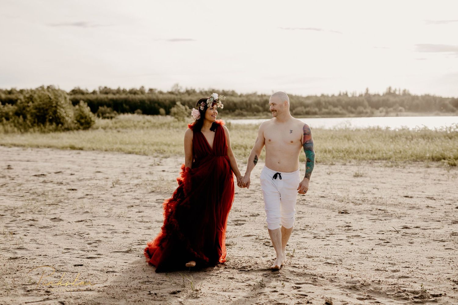 Person in flowing red dress walking along beach shoreline at sunset.
