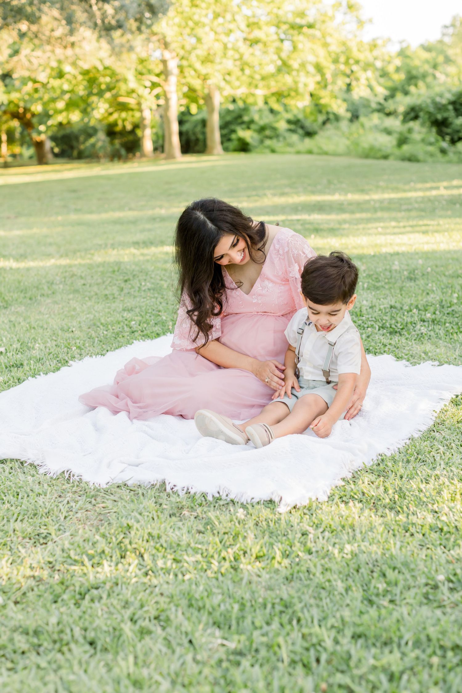 A tender maternity moment shared on a white blanket in a park setting.