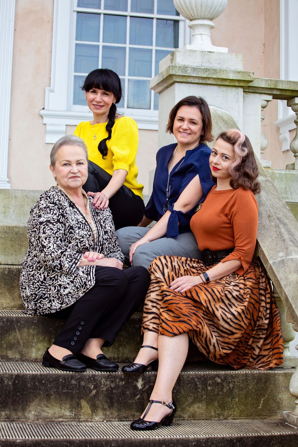 Four generations of women sit together on outdoor stone steps.