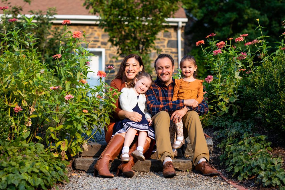 A family sits together on garden steps surrounded by blooming flowers and greenery.