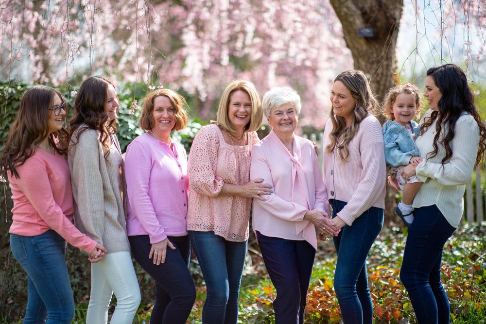 A multigenerational group stands together under blooming cherry blossoms wearing coordinated pink outfits.