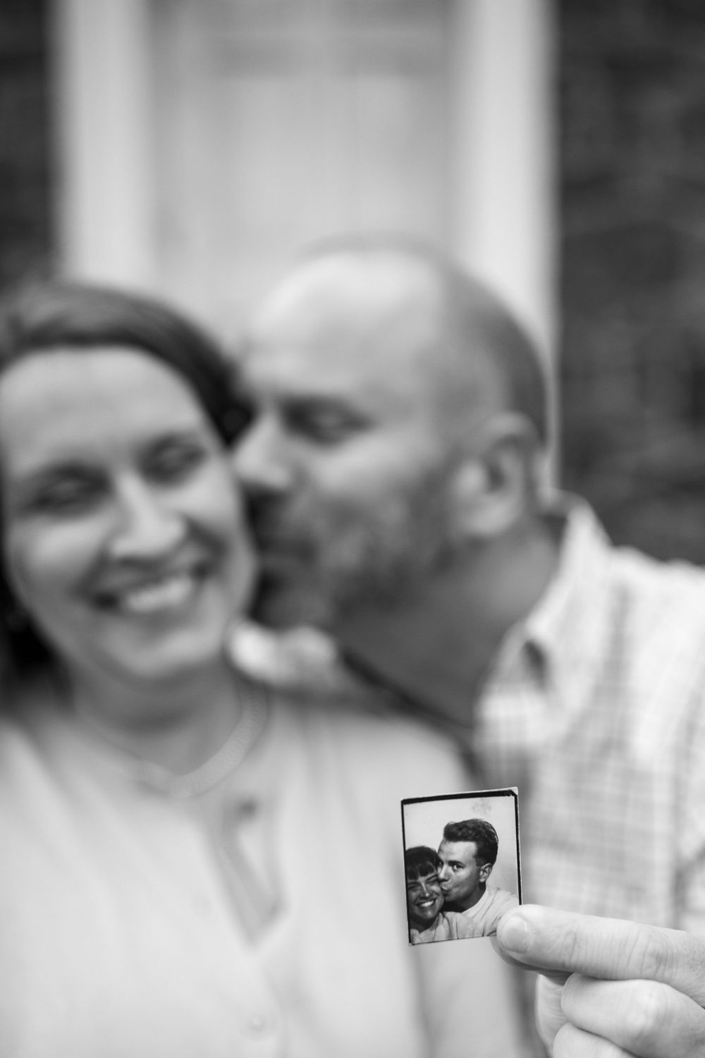 A couple shares an intimate black and white moment while holding a vintage photograph.