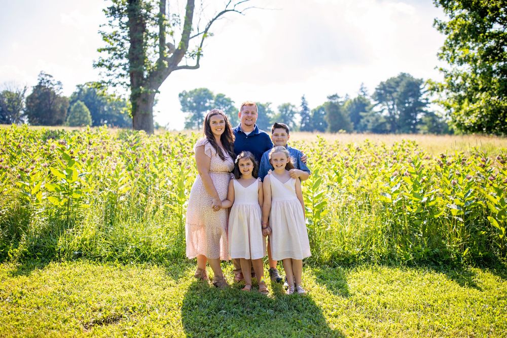 Family poses together in sunny field of yellow wildflowers.